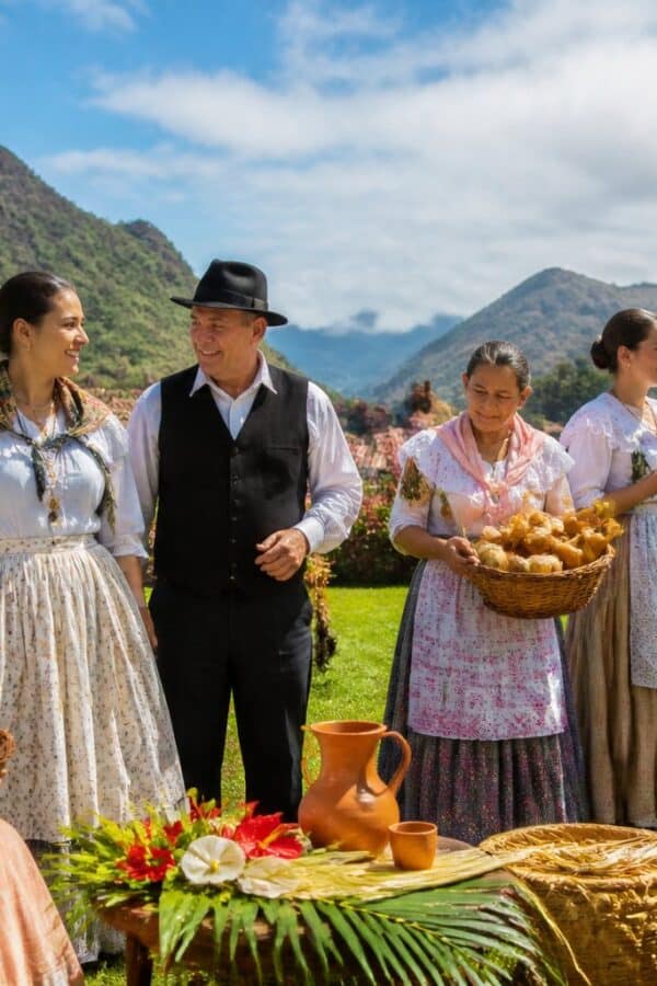 Grupo de pessoas vestindo trajes tradicionais do Espírito Santo, reunidas ao ar livre em uma paisagem verde com colinas e céu azul, participando de uma celebração cultural.