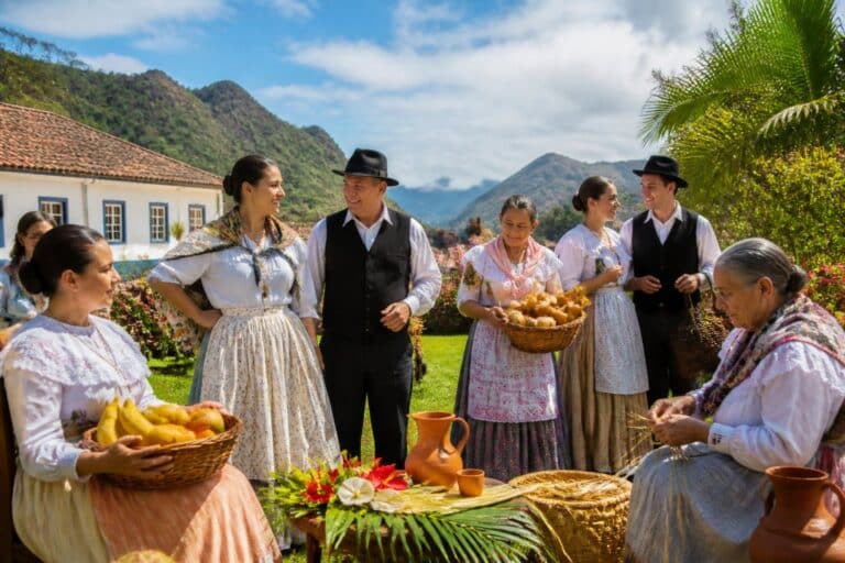 Grupo de pessoas vestindo trajes tradicionais do Espírito Santo, reunidas ao ar livre em uma paisagem verde com colinas e céu azul, participando de uma celebração cultural.