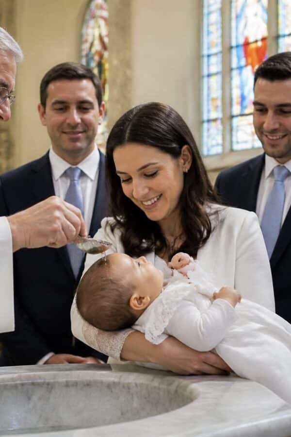 Cerimônia de batismo na igreja católica com padre, bebê vestido de branco e família reunida.
